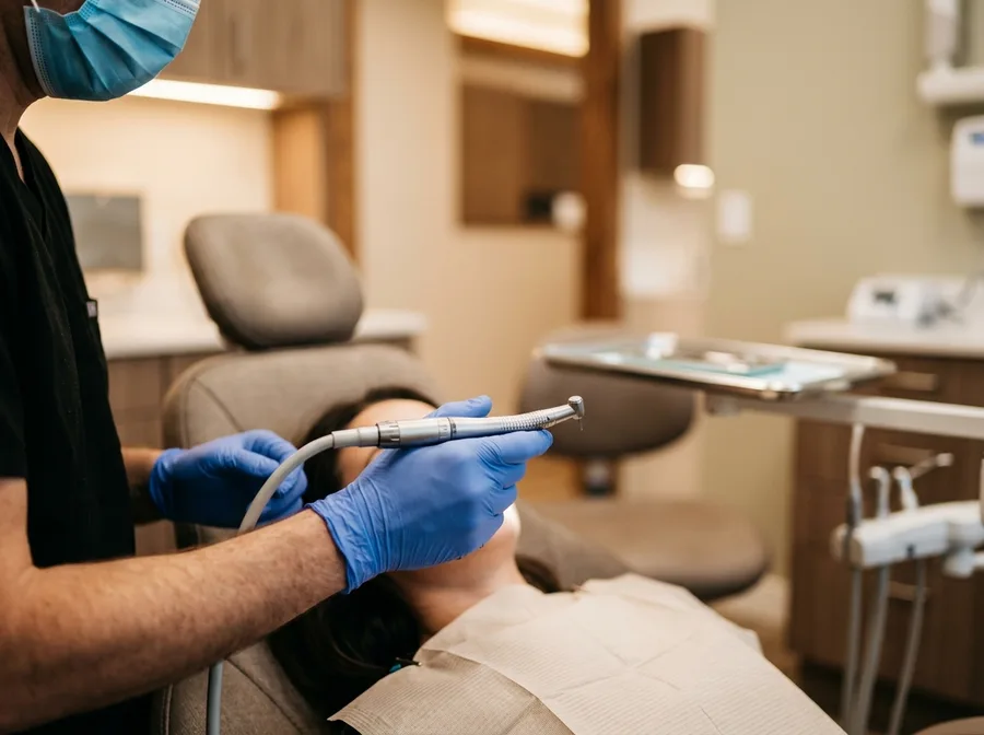 dental hygienist's gloved hands using a polishing tool near a patient's teeth, warm clinical light, close perspective on the care being done